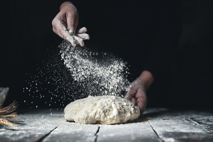 Un panadero rociando harina sobre la masa