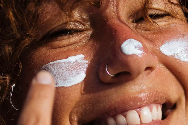 A smiling woman applying sun cream to her face
