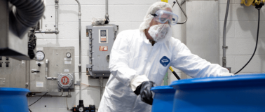 man in warehouse wearing full PPE while moving a barrel