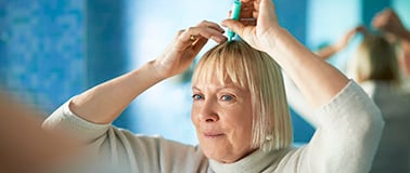 img title A woman applying a topical treatment to her scalp.